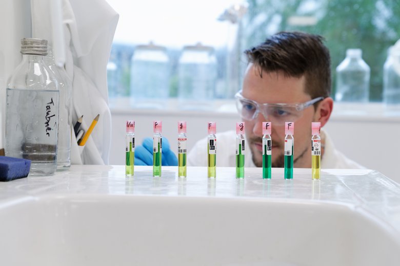 Laboratoriumflesjes met groene vloeistoffen en een onderzoeker die hiernaar kijkt in een lab