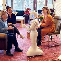 Bewoner van zorginstelling heeft interactie met sociale robot Memo, onder begeleiding van zorgmedewerker en auteur van Wintertuin -- klik op de afbeelding om te vergroten