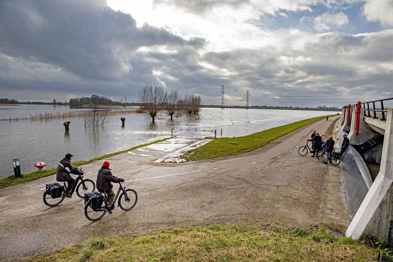 2 fietsers rijden door een polderlandschap.