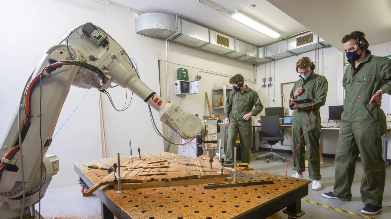 Drie mannen werken met robotarm aan hout