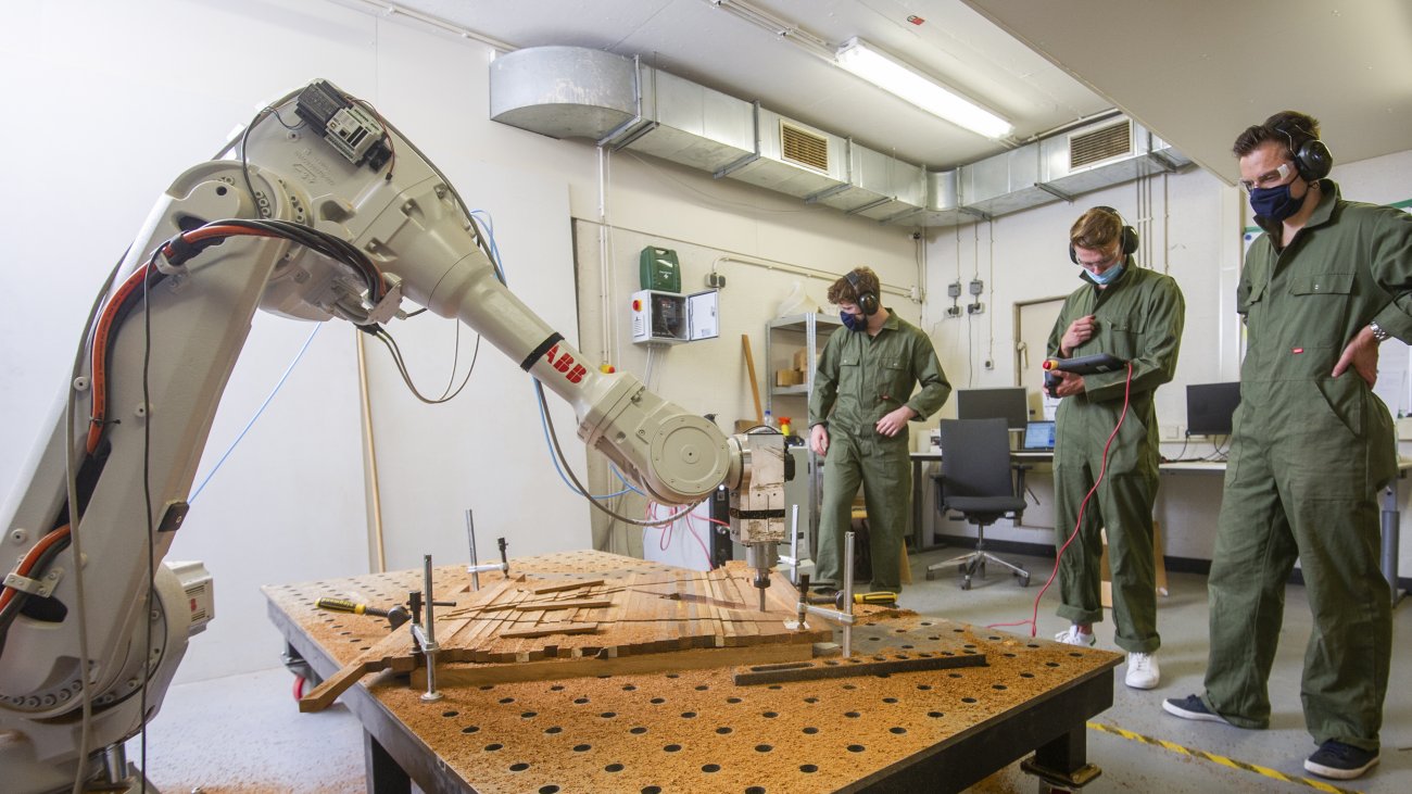 Drie mannen werken met robotarm aan hout