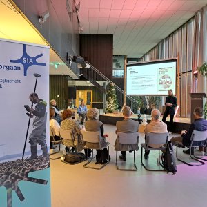 Mensen op stoelen in cirkel rondom scherm, luisterend naar DRIFT-adviseur